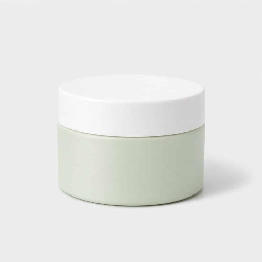 Pot de baume blanc et vert pâle posé seul sur fond neutre clair